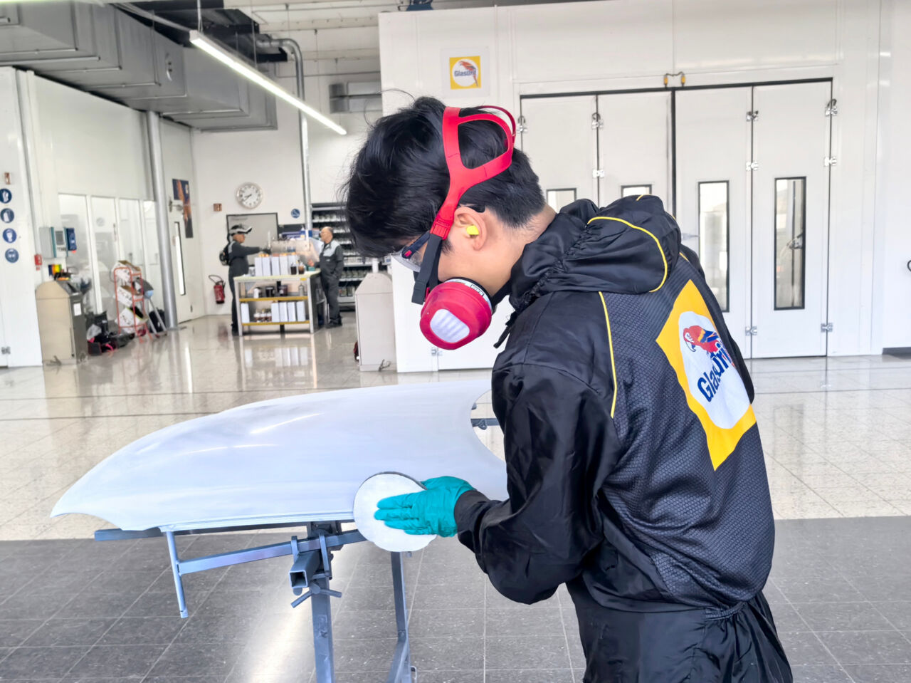 A Competitor in Car Painting works on the bodywork of a car wearing a protective mask. 
