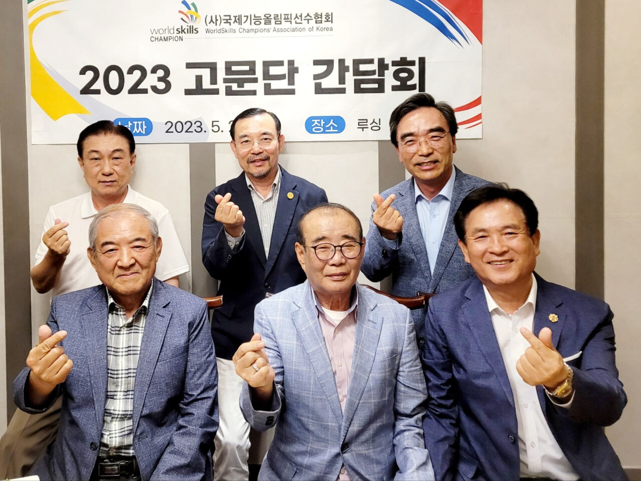 Members of the WorldSkills Champions’ Association of Korea sit in front of a banner with one arm raised.