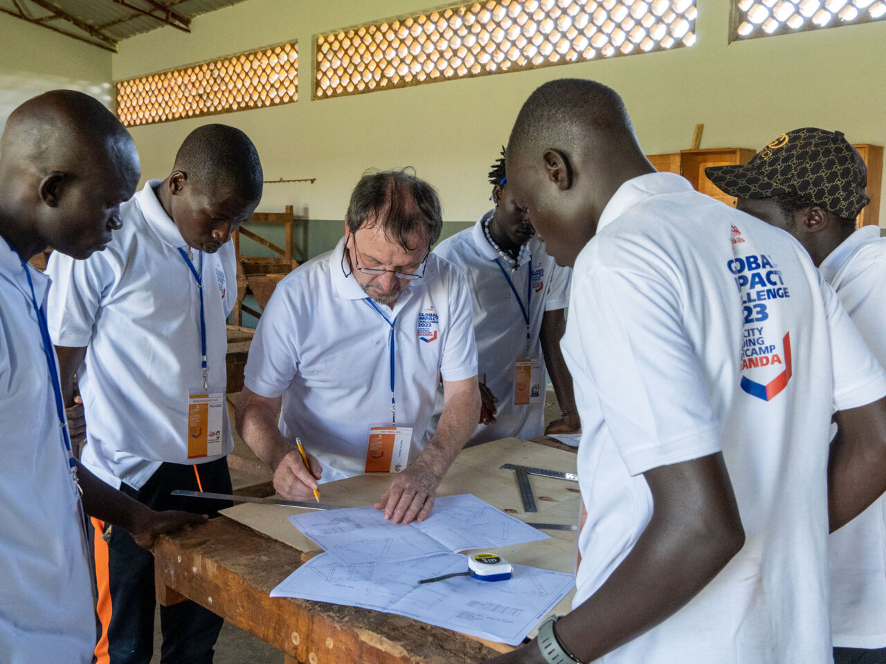 Participants of the Global Impact Challenge programme Ugandan capacity building bootcamp in May 2023 gather around a desk with a VET trainer.
