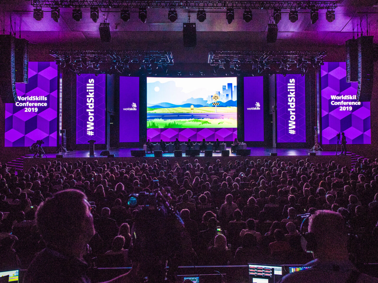 A wide shot from the back of the auditorium at WorldSkills Conference 2019 in Kazan, Kazan, Russia including audience and the stage.